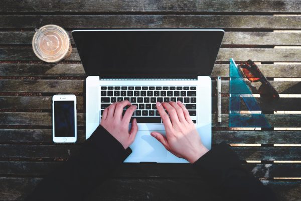 Typing on a laptop on a park bench with coffee